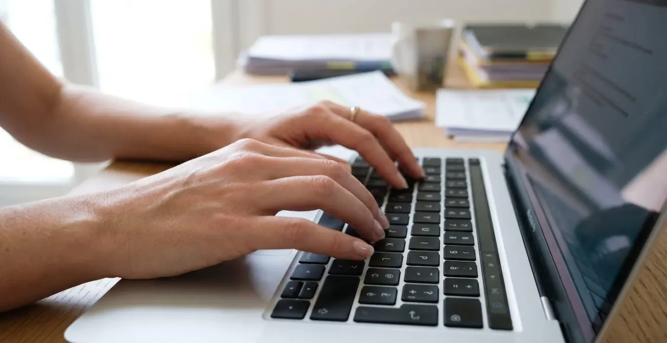 Gros plan sur des mains tapant sur un clavier d'ordinateur moderne, avec des documents comptables flous en arrière-plan