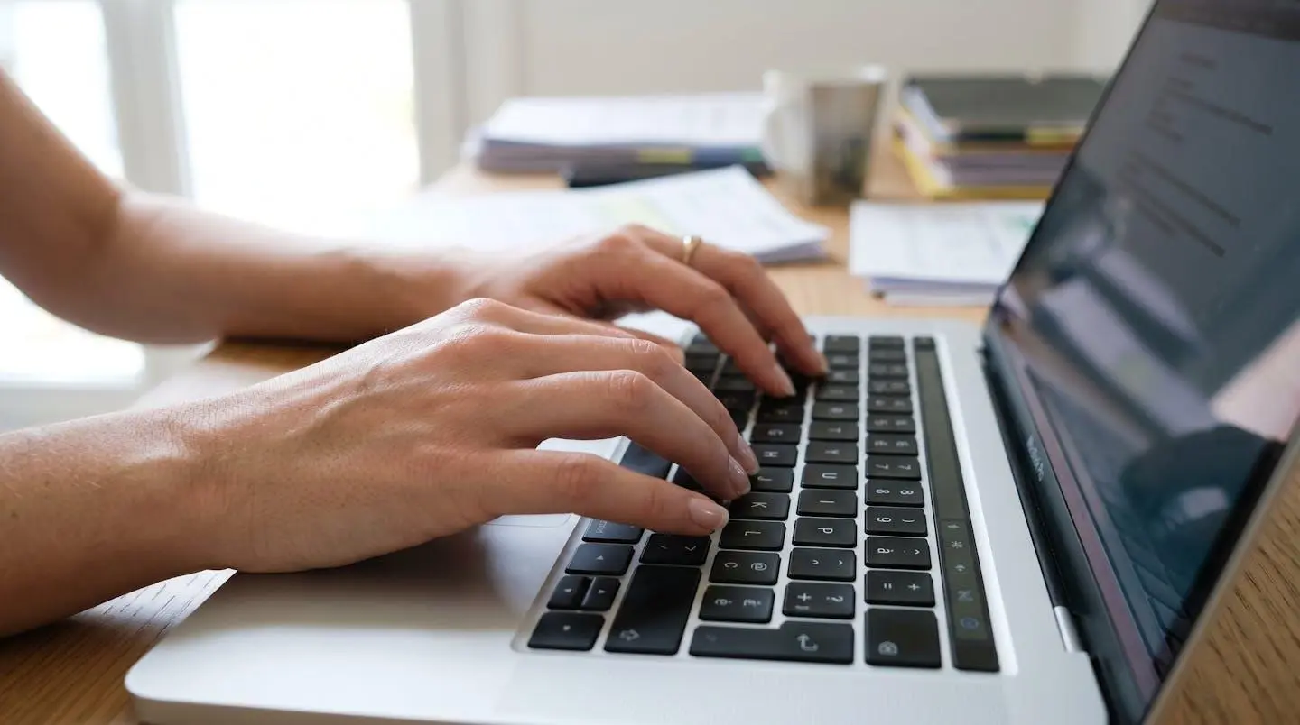 Gros plan sur des mains tapant sur un clavier d'ordinateur moderne, avec des documents comptables flous en arrière-plan